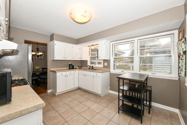 kitchen with light tile patterned flooring, stainless steel refrigerator, sink, white cabinets, and an inviting chandelier