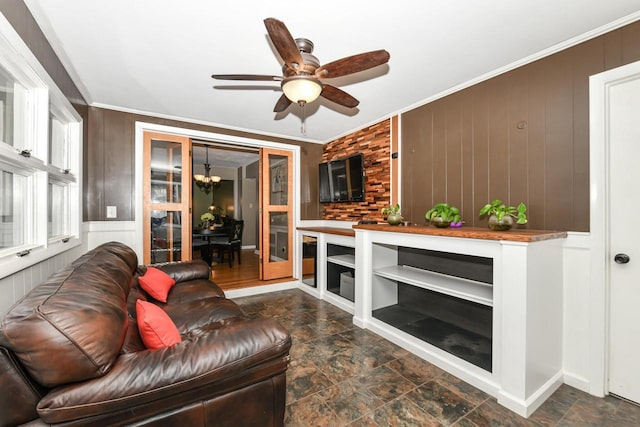 living room with ornamental molding, wooden walls, and ceiling fan with notable chandelier