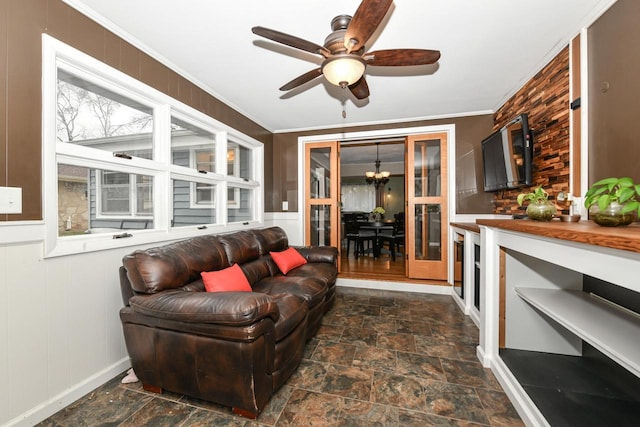 living room featuring crown molding, wooden walls, and ceiling fan with notable chandelier