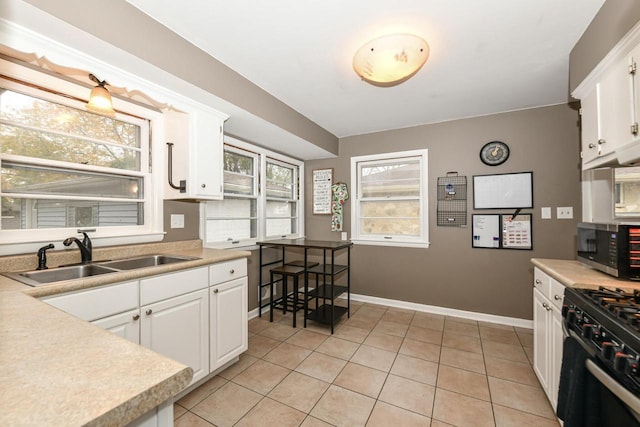 kitchen with light tile patterned flooring, range with gas stovetop, sink, and white cabinets