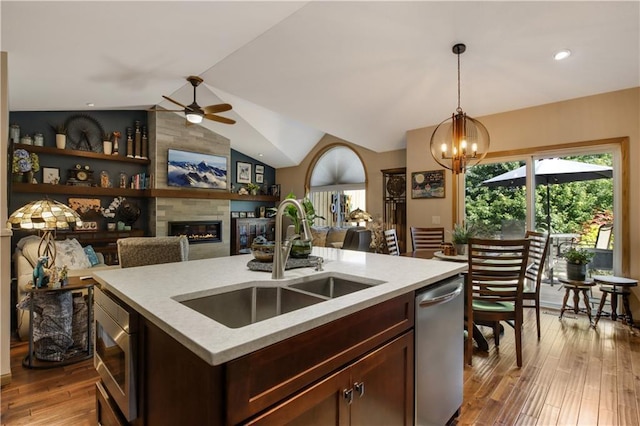 kitchen with sink, a center island with sink, appliances with stainless steel finishes, pendant lighting, and a tiled fireplace