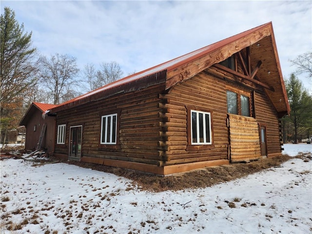 view of snow covered exterior featuring log siding and metal roof