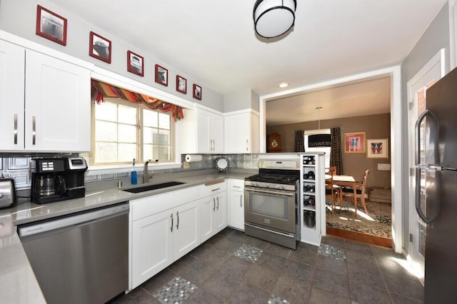 kitchen featuring decorative light fixtures, sink, dark tile patterned flooring, white cabinets, and stainless steel appliances