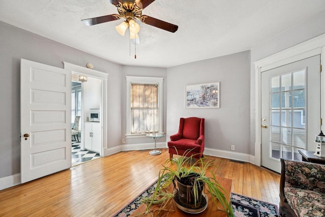 living area featuring plenty of natural light, a textured ceiling, ceiling fan, and light hardwood / wood-style flooring