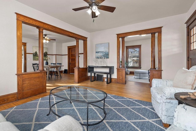 living room featuring ceiling fan, light wood-type flooring, and ornate columns