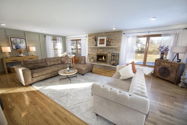 living room with a stone fireplace, light hardwood / wood-style flooring, and a wealth of natural light