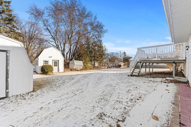 snowy yard featuring a wooden deck and a shed