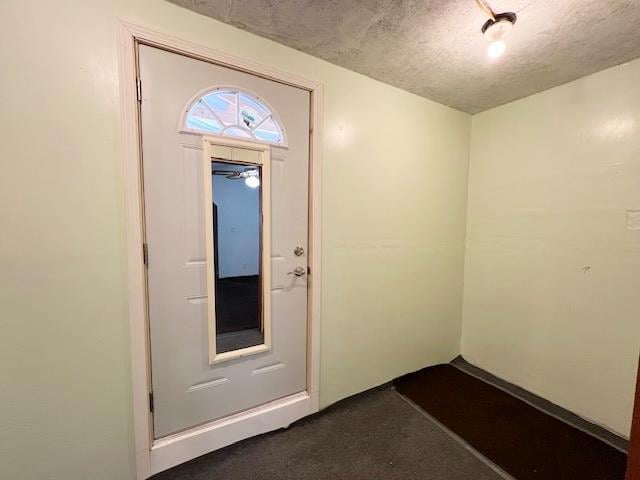 foyer with a textured ceiling and dark colored carpet