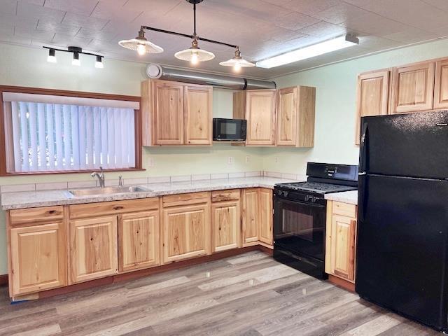 kitchen featuring pendant lighting, sink, black appliances, light stone countertops, and light wood-type flooring