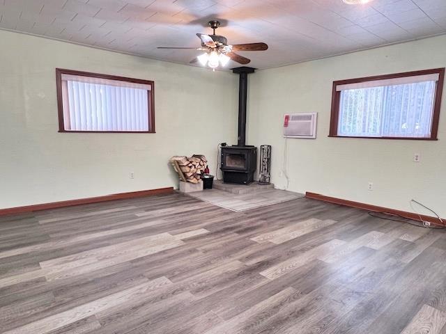 unfurnished living room with hardwood / wood-style floors, an AC wall unit, ceiling fan, and a wood stove