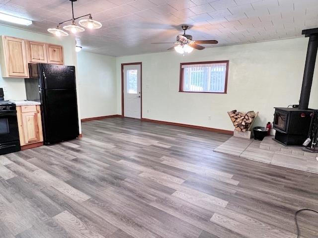 kitchen featuring pendant lighting, a wood stove, light hardwood / wood-style flooring, and black appliances