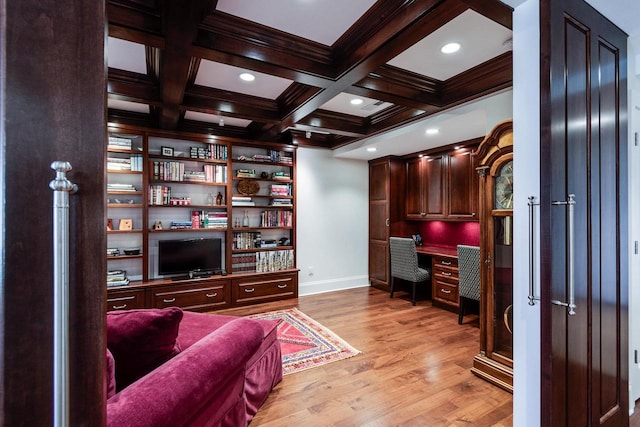 home office featuring built in desk, beamed ceiling, coffered ceiling, light wood-type flooring, and built in shelves