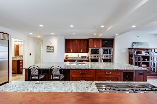 kitchen featuring a kitchen island with sink, built in appliances, light stone counters, and sink