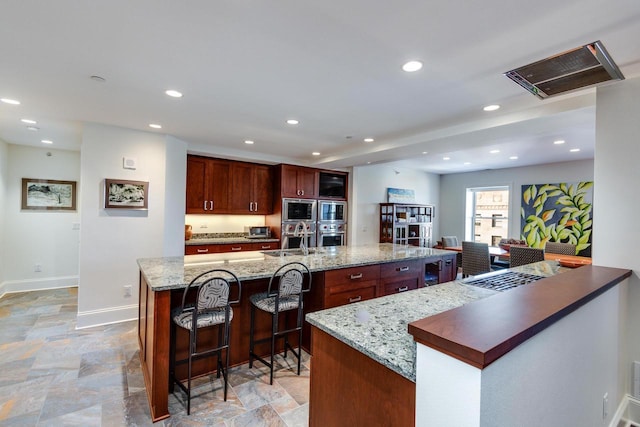 kitchen with appliances with stainless steel finishes, light stone countertops, sink, and a spacious island