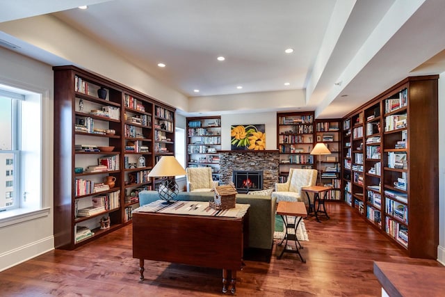 living area featuring a stone fireplace and dark wood-type flooring