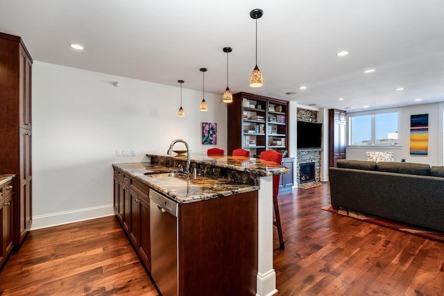 kitchen featuring sink, kitchen peninsula, a kitchen bar, stainless steel dishwasher, and dark stone counters