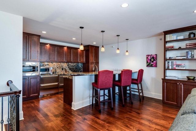 kitchen featuring light stone counters, hanging light fixtures, stainless steel microwave, a kitchen breakfast bar, and decorative backsplash