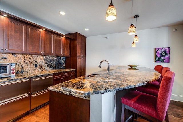 kitchen with tasteful backsplash, dark wood-type flooring, sink, and a center island with sink