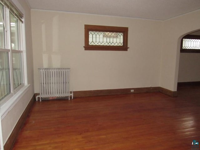 empty room with plenty of natural light, dark hardwood / wood-style floors, and radiator