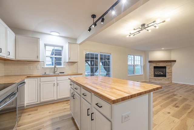 kitchen with butcher block counters, sink, white cabinets, a center island, and light hardwood / wood-style flooring