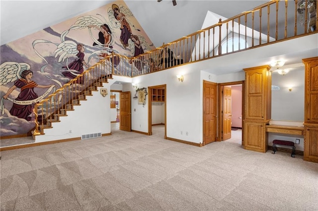 unfurnished living room with built in desk, a towering ceiling, and light carpet