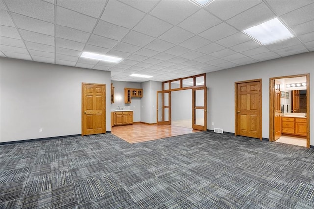 basement featuring a paneled ceiling, sink, and dark carpet