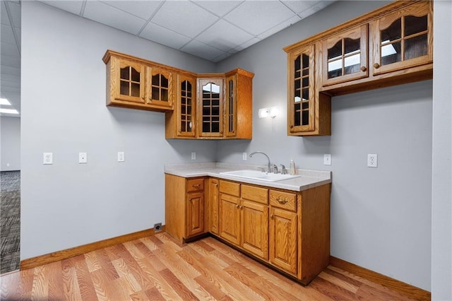 kitchen with a drop ceiling, sink, and light hardwood / wood-style flooring