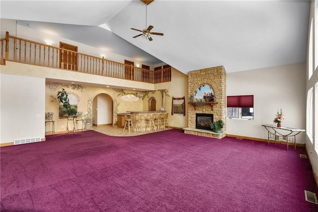 unfurnished living room with a stone fireplace, high vaulted ceiling, ceiling fan, and carpet flooring