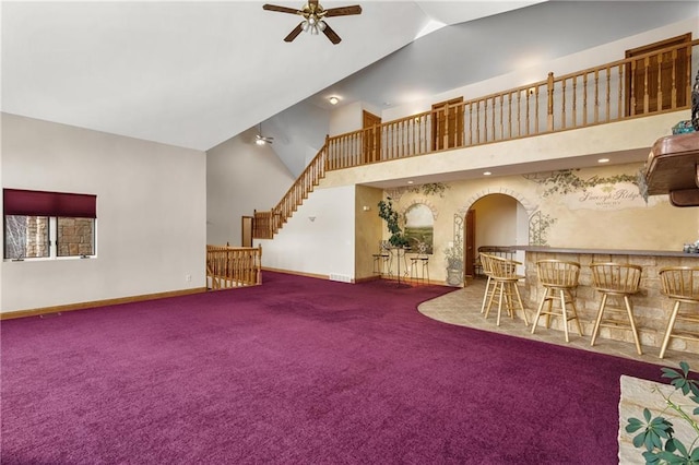 unfurnished living room with ceiling fan, carpet, bar, and high vaulted ceiling