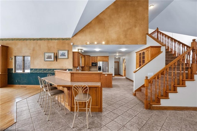 kitchen featuring a kitchen bar, high vaulted ceiling, light tile patterned flooring, stainless steel fridge with ice dispenser, and kitchen peninsula