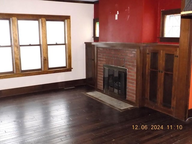 unfurnished living room featuring a brick fireplace and dark wood-type flooring