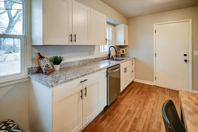 kitchen featuring dishwasher, sink, white cabinets, light stone counters, and light wood-type flooring