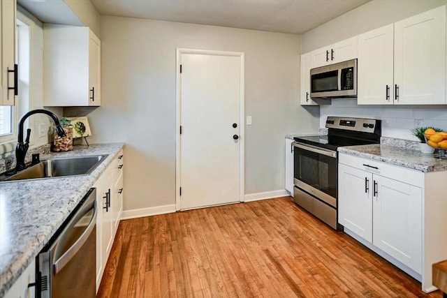 kitchen featuring appliances with stainless steel finishes, tasteful backsplash, sink, white cabinets, and light wood-type flooring