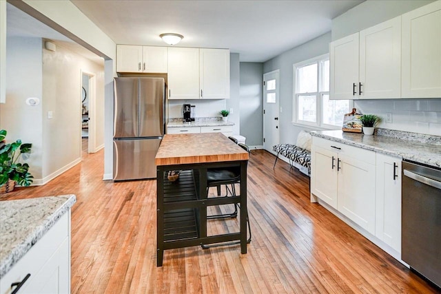 kitchen featuring light hardwood / wood-style flooring, white cabinets, stainless steel appliances, light stone countertops, and backsplash