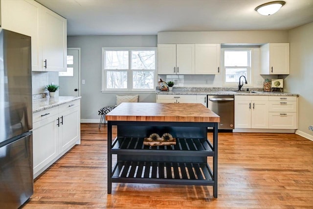 kitchen with appliances with stainless steel finishes, white cabinetry, sink, light stone counters, and light hardwood / wood-style floors