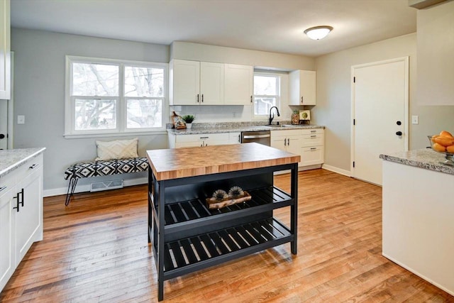 kitchen with wood counters, dishwasher, white cabinetry, sink, and light hardwood / wood-style flooring