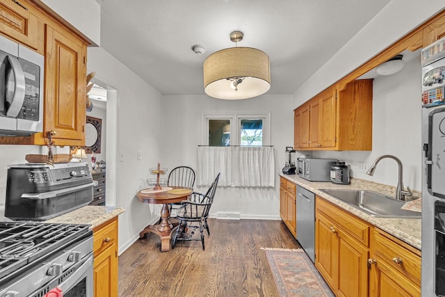 kitchen featuring decorative light fixtures, sink, dark hardwood / wood-style flooring, stainless steel appliances, and light stone countertops