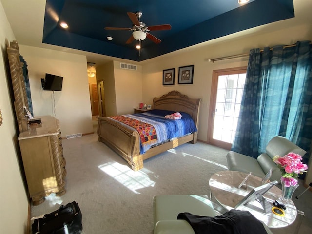 bedroom with ceiling fan, a tray ceiling, and light carpet