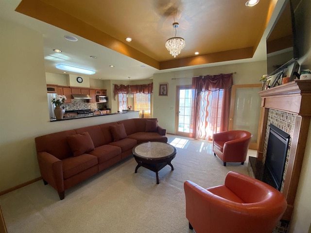 carpeted living room with a tiled fireplace, a raised ceiling, and a chandelier