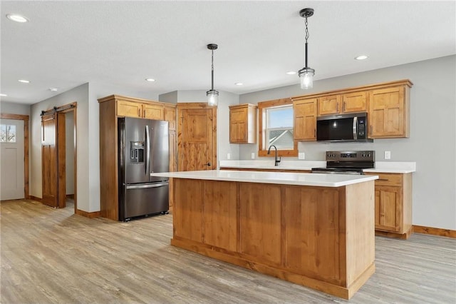 kitchen with appliances with stainless steel finishes, pendant lighting, a center island, a barn door, and light hardwood / wood-style flooring