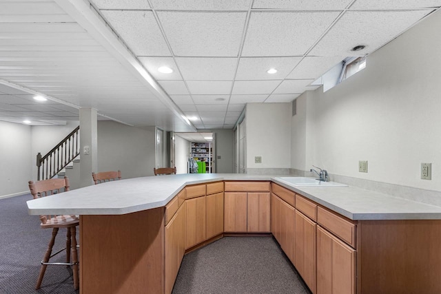 kitchen featuring sink, a paneled ceiling, a kitchen breakfast bar, carpet floors, and kitchen peninsula