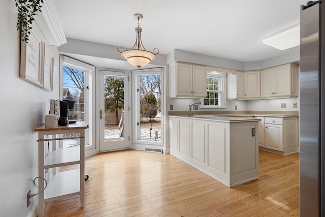 kitchen featuring sink, stainless steel fridge, hanging light fixtures, cream cabinets, and light wood-type flooring