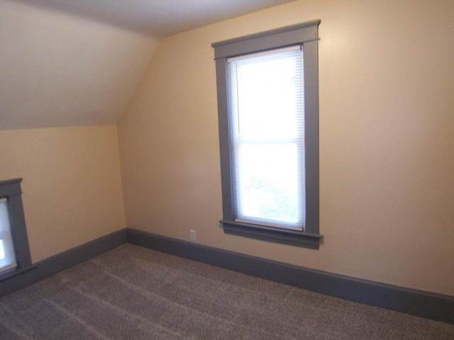 additional living space with lofted ceiling, a healthy amount of sunlight, and dark carpet