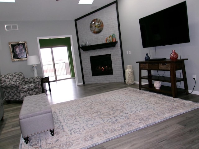 living room featuring a brick fireplace, dark wood-type flooring, and a skylight