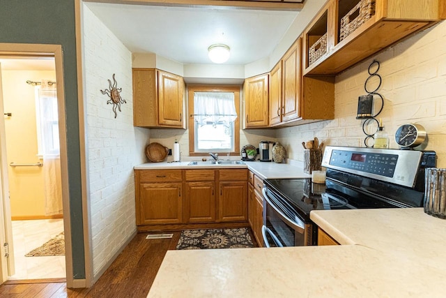 kitchen featuring dark wood-type flooring, stainless steel range with electric stovetop, brick wall, and sink