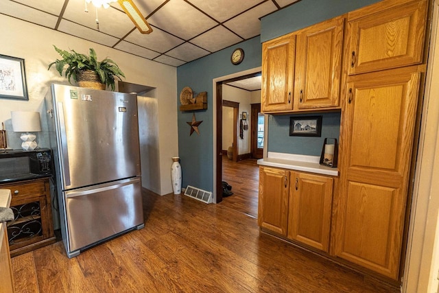 kitchen with stainless steel refrigerator, dark hardwood / wood-style flooring, and a drop ceiling