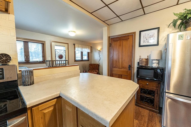 kitchen with appliances with stainless steel finishes, dark wood-type flooring, and a paneled ceiling