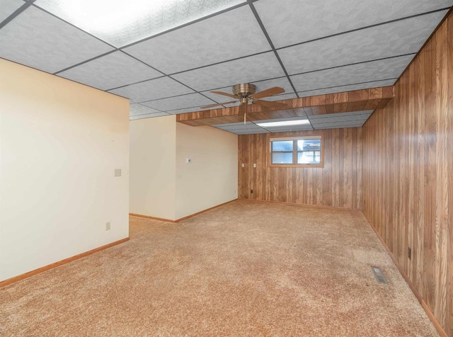 basement featuring light colored carpet, ceiling fan, and wood walls