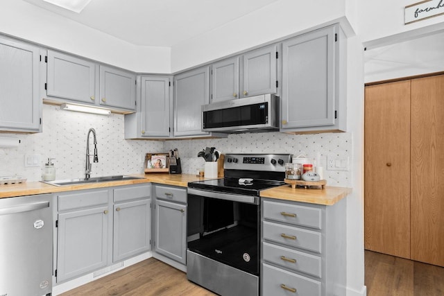 kitchen with sink, gray cabinetry, stainless steel appliances, hardwood / wood-style floors, and backsplash