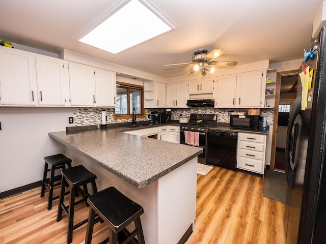 kitchen featuring black appliances, white cabinets, a kitchen bar, and kitchen peninsula